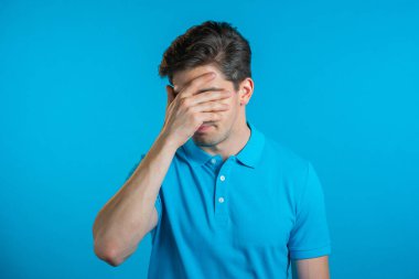 Genç bir adamın facepalm hareketi yaparken portresi, hayır, unuttum. Mutsuz adam üzüntü, pişmanlık, drama, başarısızlık hissediyor. Mavi duvarda izole edilmiş.