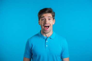 İnsan şaşkınlığı tasvir eder, zevkli yüz efektini gösterir. Şaşırmış, heyecanlı, mutlu adam. Mavi arka planda yakışıklı erkek şok modeli.