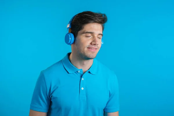 英俊的年轻男子，有时髦的发型，有乐趣，微笑与耳机在工作室蓝色背景。音乐、舞蹈、无线电概念. — 图库照片