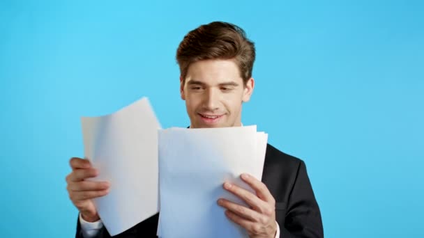 Giovane bell'uomo in giacca e cravatta controlla documenti, bollette, rapporto. Uomo d'affari isolato su sfondo blu. È soddisfatto di lavoro di personale corporativo. — Video Stock