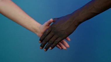Siyah erkek ve beyaz kadının elleri. El sıkışın, yakın plan. Irklar arası arkadaşlık, ırkçılık karşıtlığı, kardeşlik, işbirliği konsepti. Mavi stüdyo arka planında izole edilmiş. Etnik çeşitlilik - Irksal eşitlik.
