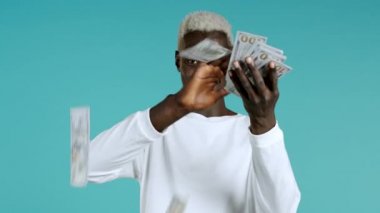 Melez ırk adamı ve mutlu yüz etrafa para saçıyor. İnsanlar Amerikan paralarını fazla harcıyor. Afrikalı adam mavi stüdyo arka planında dolarlarla dolu..