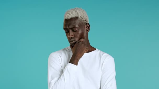 Denkende hippe Afrikaanse man die op en neer kijkt op een blauwe achtergrond. Pensieve gezichtsuitdrukkingen. Knappe man zwart model. — Stockvideo
