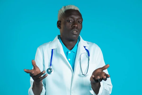 Portrait of unsure african doctor in professional medical white coat shrugs his arms, makes gesture of I dont know, care. Body language. Doc man.