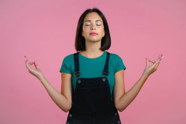 Esmer saçlı, sakin, meditasyon yapan hippi kadın. Kız sakinleşiyor, pembe stüdyo arka planında derin derin nefes alıyor.