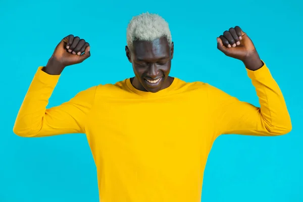 Homem africano dançando positivo no fundo do estúdio azul. Bonito homem afro preto modelo cara em amarelo. Festa, felicidade, liberdade, conceito de juventude. — Fotografia de Stock