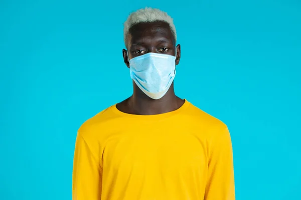 Portrait de bel homme afro-américain masqué regardant vers la caméra. Le gars en studio sur fond bleu vif. Arrêter le concept de virus, protection bactérienne. — Photo