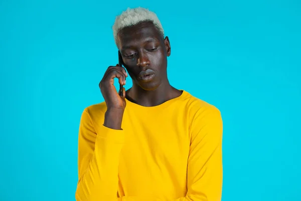 El joven afro habla en serio por teléfono. Un tipo sosteniendo y usando un teléfono inteligente. Fondo estudio azul. — Foto de Stock