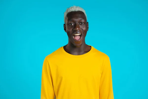 Hombre africano representa asombro, muestra WOW deleite efecto de la cara. Sorprendido chico feliz emocionado. Hermoso modelo chocado masculino sobre fondo azul. — Foto de Stock
