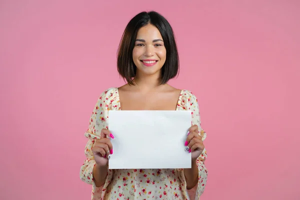 Retrato de mujer joven sosteniendo papel a4 horizontal blanco aislado sobre fondo de estudio rosa. Copiar espacio. —  Fotos de Stock