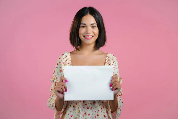 Retrato de jovem segurando papel a4 horizontal branco isolado no fundo do estúdio rosa. Espaço de cópia. — Fotografia de Stock