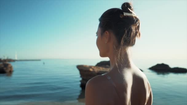 Mladá žena kráčí podél moře po skalnaté pláži. Dívka na tropické dovolené. Luxusní cíl. Cestování, příroda, letní koncept. Zpomalený pohyb. — Stock video