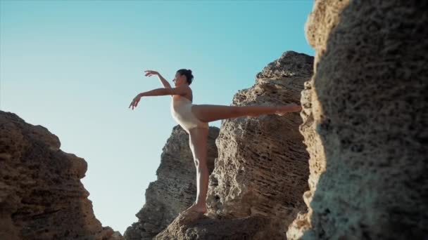 Bailarina bailando entre rocas cerca del océano o el mar al amanecer o al atardecer. Retrato de mujer flexible practicando en ejercicios clásicos. Concepto de ternura, ligereza, arte y talento en la naturaleza — Vídeos de Stock