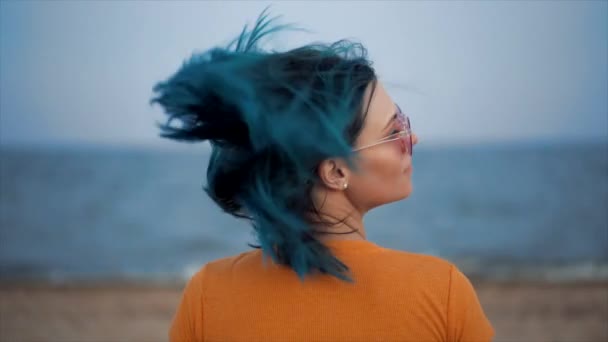 Neobvyklá žena třese modrými barvenými vlasy na pozadí mořské pláže. Portrét hipster dívka s jedinečným módním účesem, ona se těší v létě sama, demonstrovat její svěží barvu. — Stock video