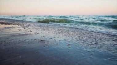 Gün batımında deniz dalgaları. Kumlu sahilde güzel fırtınalı hava. Kamera suya mümkün olduğunca yakın çekim yapar. Nefes kesici bir manzara. Yavaş çekim. 