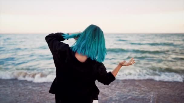Neobvyklá žena s modře obarvenými vlasy tančící, točící se rukama na mořském pozadí. Ženskost, dovolená, vitalita, zdravý životní styl. Holka se baví, směje. — Stock video