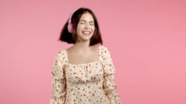 Müzik dinleyen, pembe stüdyo arka planında kulaklıklarla dans eden çekici bir kadın. Güzel kız portresi. Radyo, mutluluk, özgürlük, gençlik kavramı.