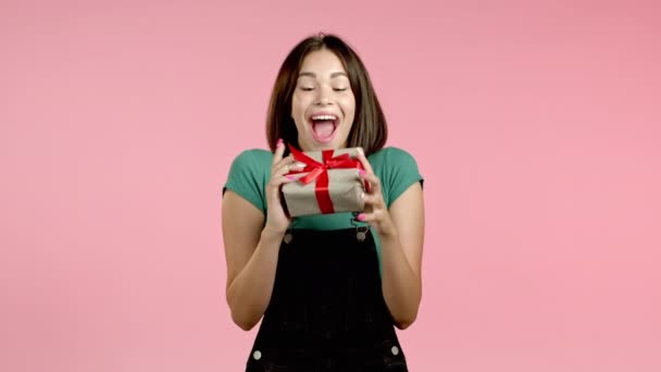 Femme excitée reçu boîte cadeau avec arc. Elle est heureuse et flattée par l'attention. Fille souriant avec présent sur fond rose. Portrait studio — Video