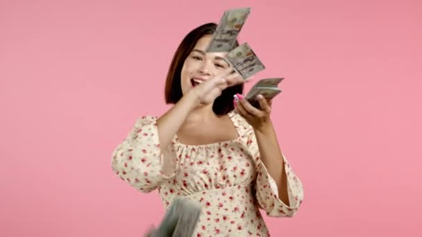 Pretty woman with happy face scatters, waste money. Girl overspend US currency. Lady is flush with dollars on pink studio background . — Stock Video