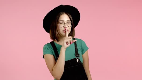 Hipster-Frau mit Hut hält Finger auf den Lippen über rosa Hintergrund. Geste von shhh, Geheimnis, Schweigen. Nahaufnahme. — Stockvideo