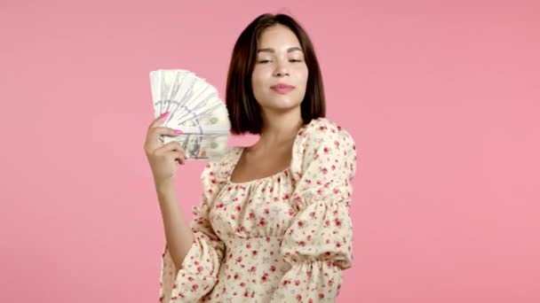 Şaşırtıcı derecede mutlu, heyecanlı bir kadın pembe duvarda Amerikan doları banknotları gösteriyor. Başarı, kazanç, zafer sembolü. — Stok video