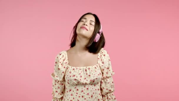 Ελκυστική γυναίκα χορεύει ακούγοντας μουσική, χορεύει με ακουστικά σε ροζ φόντο στούντιο. Ωραίο πορτραίτο κοριτσιού. Ραδιόφωνο, ευτυχία, ελευθερία, έννοια της νεολαίας. — Αρχείο Βίντεο