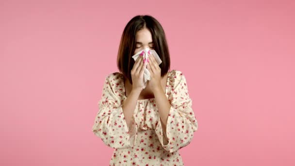 Жінка чхає в тканину. Ізольована дівчина на рожевому фоні студії. Леді хвора, у неї холодна або алергічна реакція. Коронавірус, епідемія 2020, хвороба — стокове відео