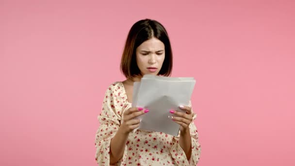 Занепокоєна сердита жінка тримає папери, розсіює їх ізольовано на рожевому тлі. Красива дівчина перевіряє документи, рахунки за комунальні послуги . — стокове відео