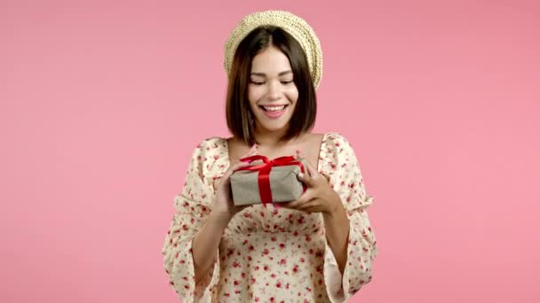 흥분 한 여자는 활이 달린 선물 상자를 받았다. 아내는 관심을 받으면 행복 해 하고 기분이 좋아 집니다. 분홍색 배경에 밝게 웃는 소녀. 스튜디오 사진 — 비디오