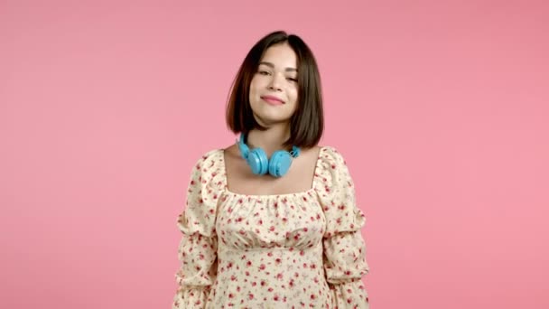 Mulher atraente dançando com fones de ouvido no fundo do estúdio rosa. Retrato bonito da menina. Música, rádio, felicidade, liberdade, conceito de juventude. — Vídeo de Stock