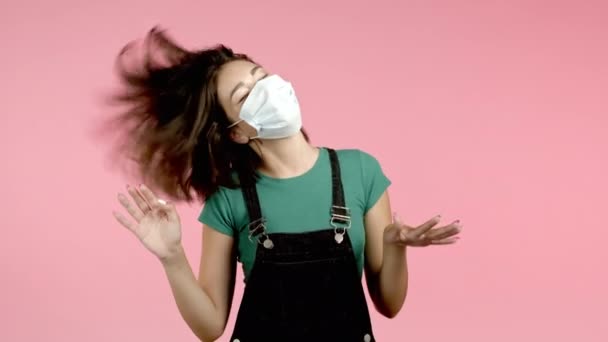 Mooie vrouw in beschermende medische masker dansen energiek en actief op roze studio achtergrond. Schattig meisjes portret. Feest, geluk, vrijheid, jeugdconcept. — Stockvideo