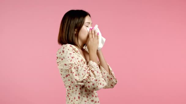 Жінка чхає в тканину. Ізольована дівчина на рожевому фоні студії. Леді хвора, у неї холодна або алергічна реакція. Коронавірус, епідемія 2020, хвороба — стокове відео