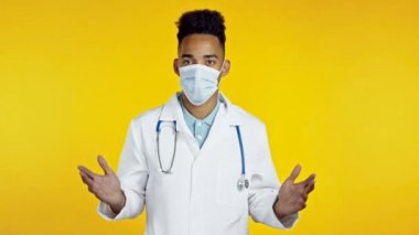 Profesyonel medikal beyaz önlüklü Afrikalı doktor portresi kollarını silkiyor, ne bileyim, umursadığını gösteriyor. Vücut dili. Sarı stüdyo geçmişindeki doktor..