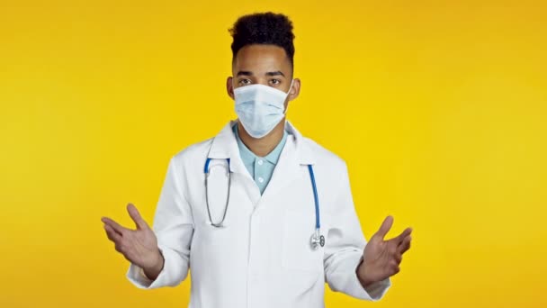 Portrait of unsure african doctor in professional medical white coat shrugs his arms, makes gesture of I don 't know, care. Bahasa tubuh. Doc pria di latar belakang studio kuning. — Stok Video