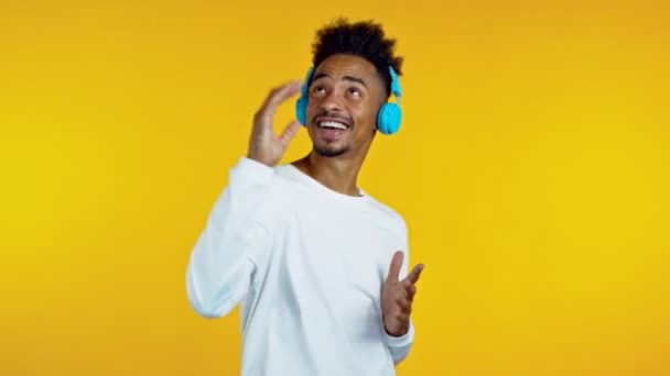 Beau Africain qui s'amuse, dansant avec des écouteurs bleus dans un studio jaune. Musique, danse, concept radio, ralenti — Video