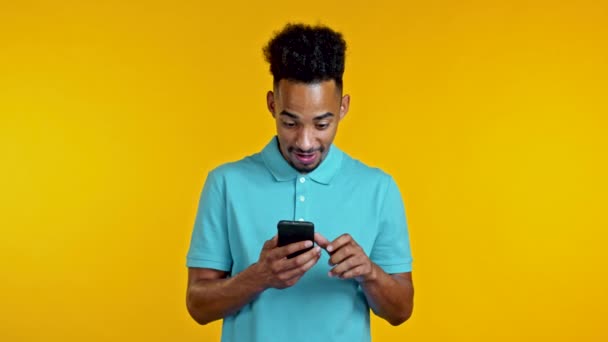 Hombre negro guapo recibe notificación feliz en el teléfono móvil. Se regocija. Tecnología, éxito, victoria, concepto de felicidad. — Vídeos de Stock