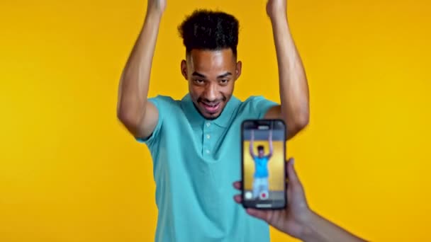 Vlogger souriant homme africain enregistrement vidéo de lui-même danser devant la caméra smartphone sur fond jaune. Influenceur fait drôle clip de médias sociaux — Video