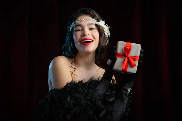 Joyful vintage woman dressed in Art Deco style holding gift box with bow on velours background. She is glad to get present. retro, party, fashion concept. — Stock Photo, Image