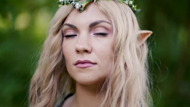 Ritratto di giovane donna in abiti da elfo cosplay e con trucco su sfondo verde. Look fantastico, lunghi capelli biondi, corona della foresta. Concetto Halloween. — Video Stock