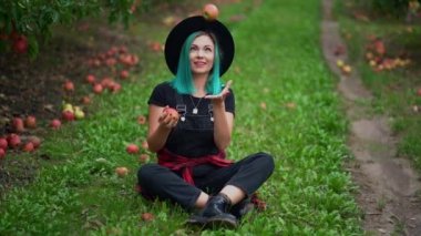 Mavi saçlı hippi kadın sonbahar mevsiminde bahçede oturmuş olgun kırmızı elmalarla hokkabazlık yapıyor. Neşeli kız gülümsüyor. Organik, doğa konsepti.
