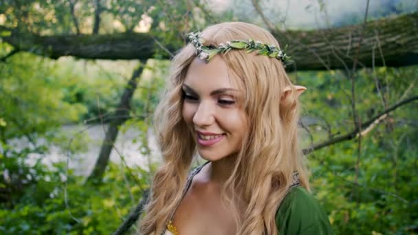 Kostümlü genç kadın portresi elf kıyafetleri ve yeşil arka planda makyajlı. Muhteşem görünüş, uzun sarı saç, orman tacı. Cadılar Bayramı konsepti. — Stok video