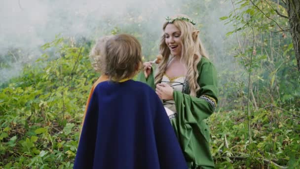 Fairy elf cosplay młoda kobieta traktuje małych chłopców hobbitów cukierki w zielonym lesie. Koncepcja Halloween, postaci z bajek, dzieci. — Wideo stockowe