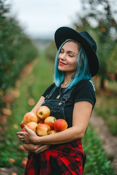 La donna dai capelli azzurri ha raccolto molti frutti di mela rossa maturi da albero in giardino verde. Stile di vita biologico, agricoltura, occupazione giardiniere — Foto Stock