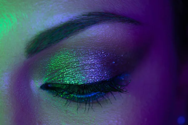 Extreme close up of female eye iris under neon light. Woman with beautiful makeup, glitter shadows and false lashes. Girls green eye. Nightlife, night club concept. — Stock Photo, Image