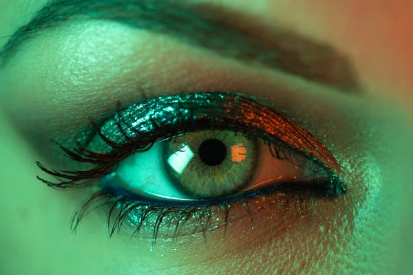 Extrem närbild av kvinnliga ögat iris under neon ljus. Kvinna med vacker makeup, glitter skuggor och lösögonfransar. Flickor gröna ögat. Nattliv, nattklubbskoncept. — Stockfoto