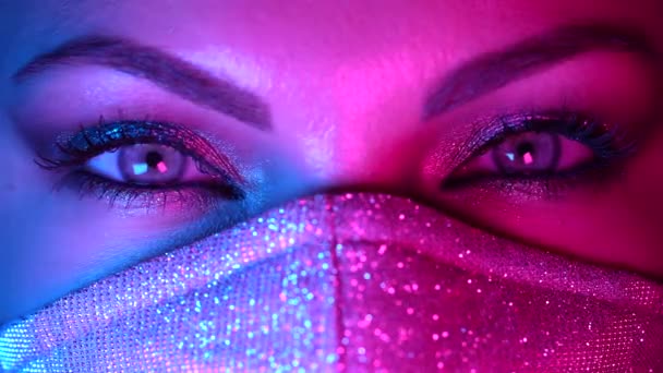 Ženy tvář v třpytivé ochranné masce, úžasné různé make-up pod neonové barevné světlo. Žena se zářícími stíny. Glamour, art, beauty, fashion, pandemic, covid-19 concept. — Stock video