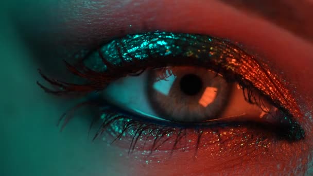 Extreme close-up van het menselijk oog iris onder neon licht. Vrouw met mooie make-up, glitter schaduwen. Womens groen oog samentrekken. Schoonheid, cosmetica, nachtclub lifestyle concept. — Stockvideo