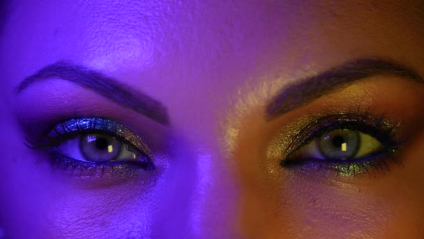 Close up of human eyes iris under neon light. Female with beautiful makeup, glitter shadows and false lashes. Womens green eyes contracting. Nightlife, night club concept. — Stock Video