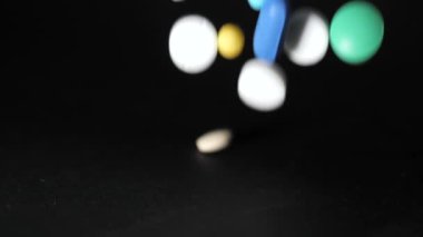 Eczane temalı. Kara Masa 'nın üzerinde çok renkli izole haplar ve kapsüller. Vitaminler karanlık yüzeye düşüyor. Yavaş çekim.