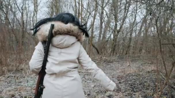 Κυνηγός γυναίκα φοράει ζεστό παλτό και τρέχει με τουφέκι στο δάσος του φθινοπώρου. Νεαρό αγνώριστο κορίτσι εκπαιδεύεται με όπλο στην περιοχή της μάχης. Αργή κίνηση. Πίσω όψη. — Αρχείο Βίντεο